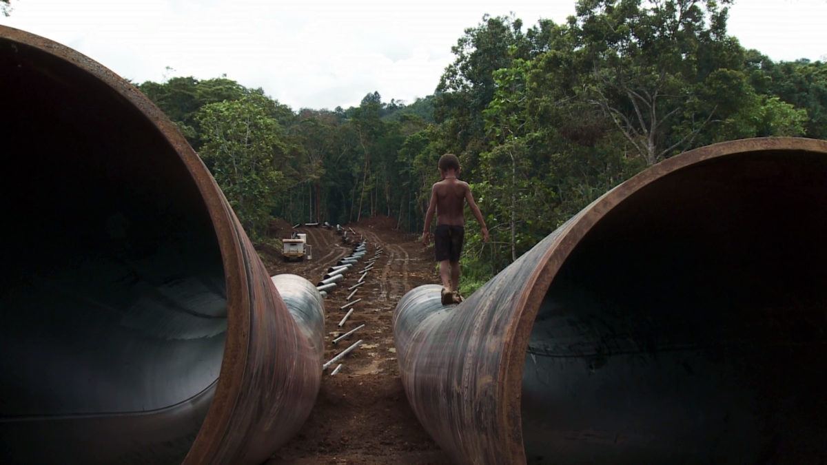 A young boy walking on top of a large pipe next to another large pipe