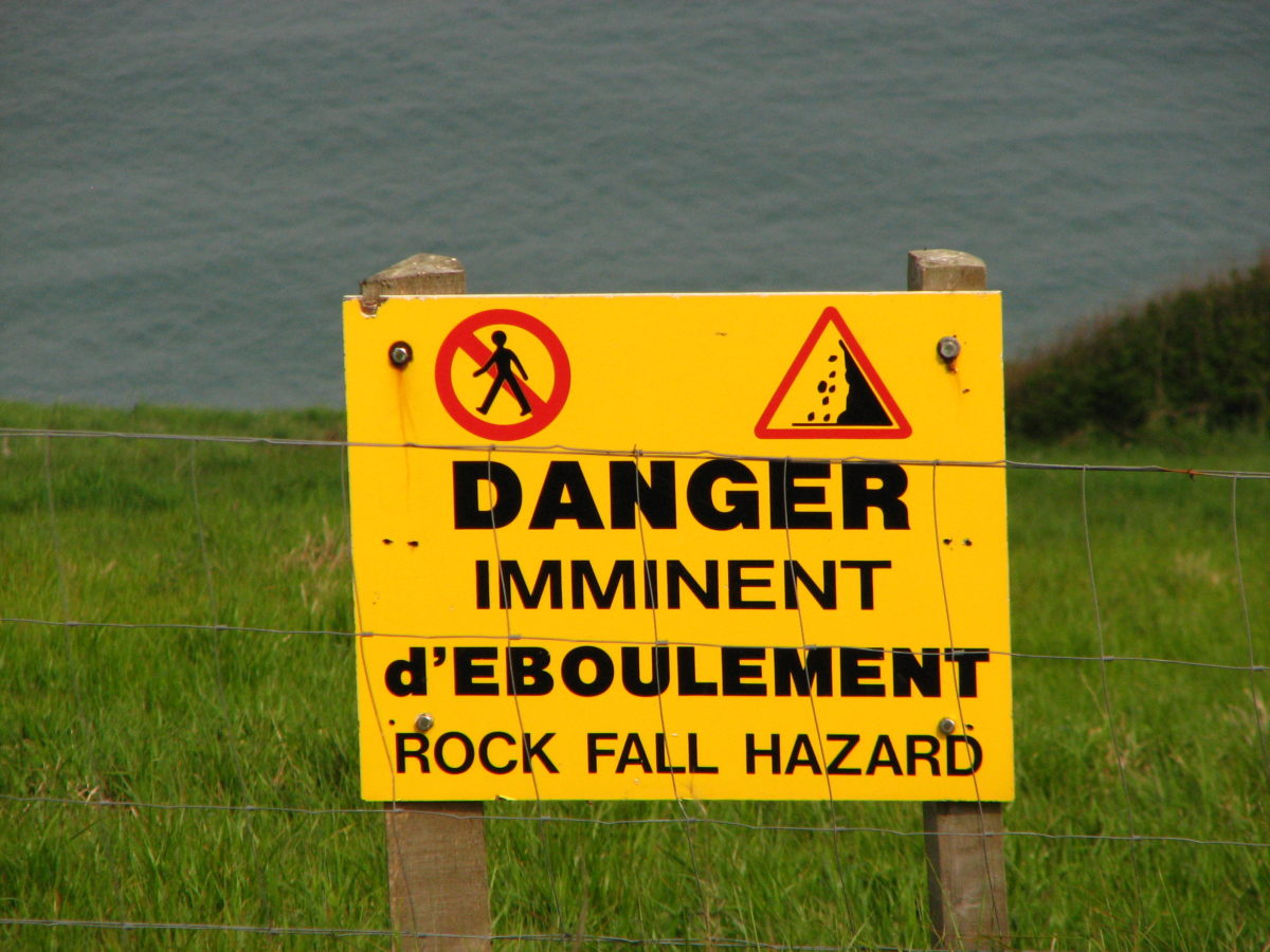 Warning sign next to a body of water warning of falling rocks