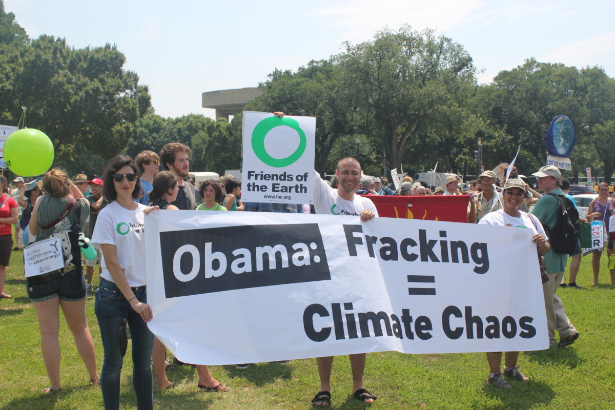 Three anti-fracking activists hold a banner that states "Obama: fracking = climate chaos" and a Friends of the Earth sign