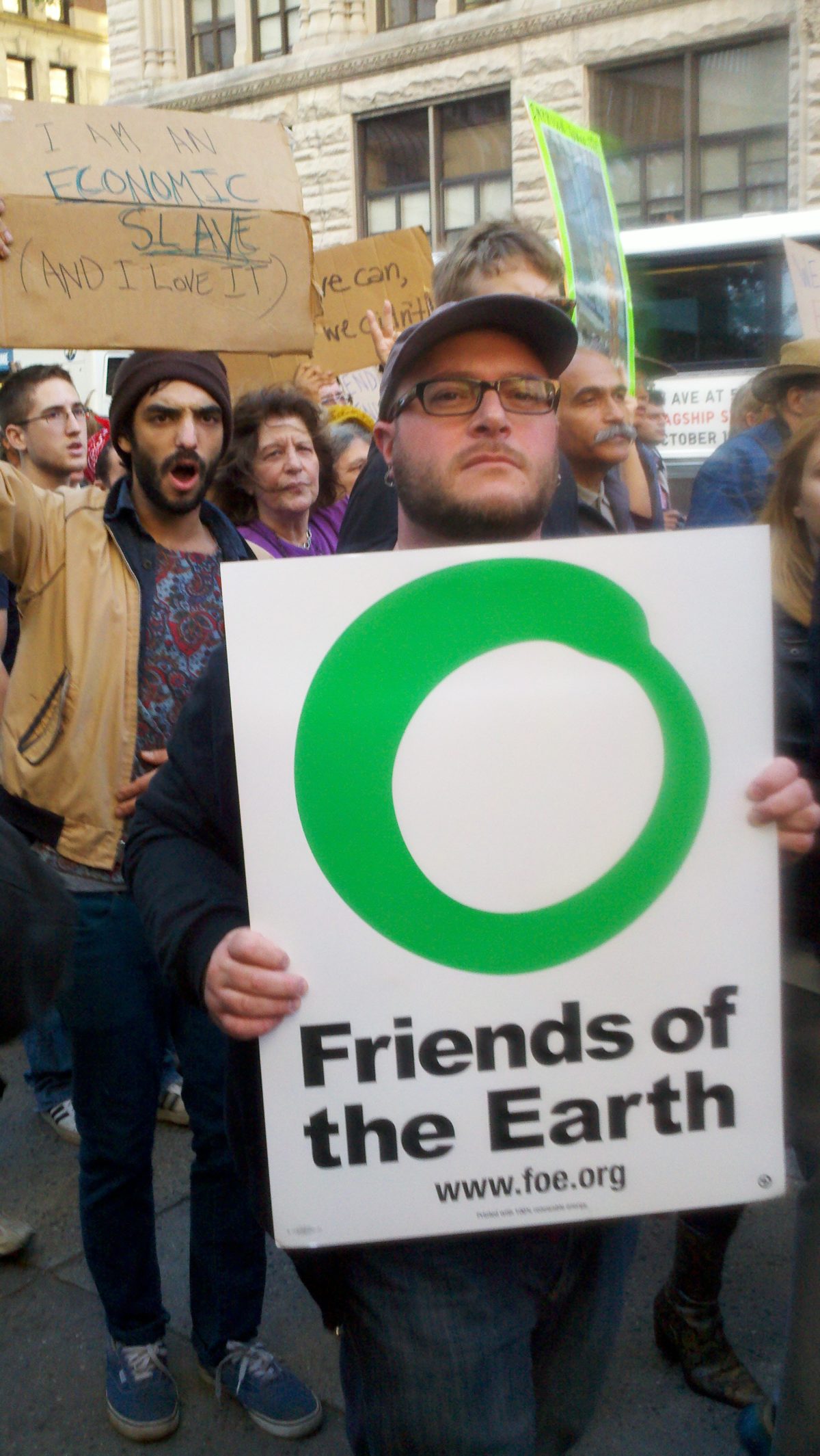 A protestor with a Friends of the Earth sign standing in a group of other protestors