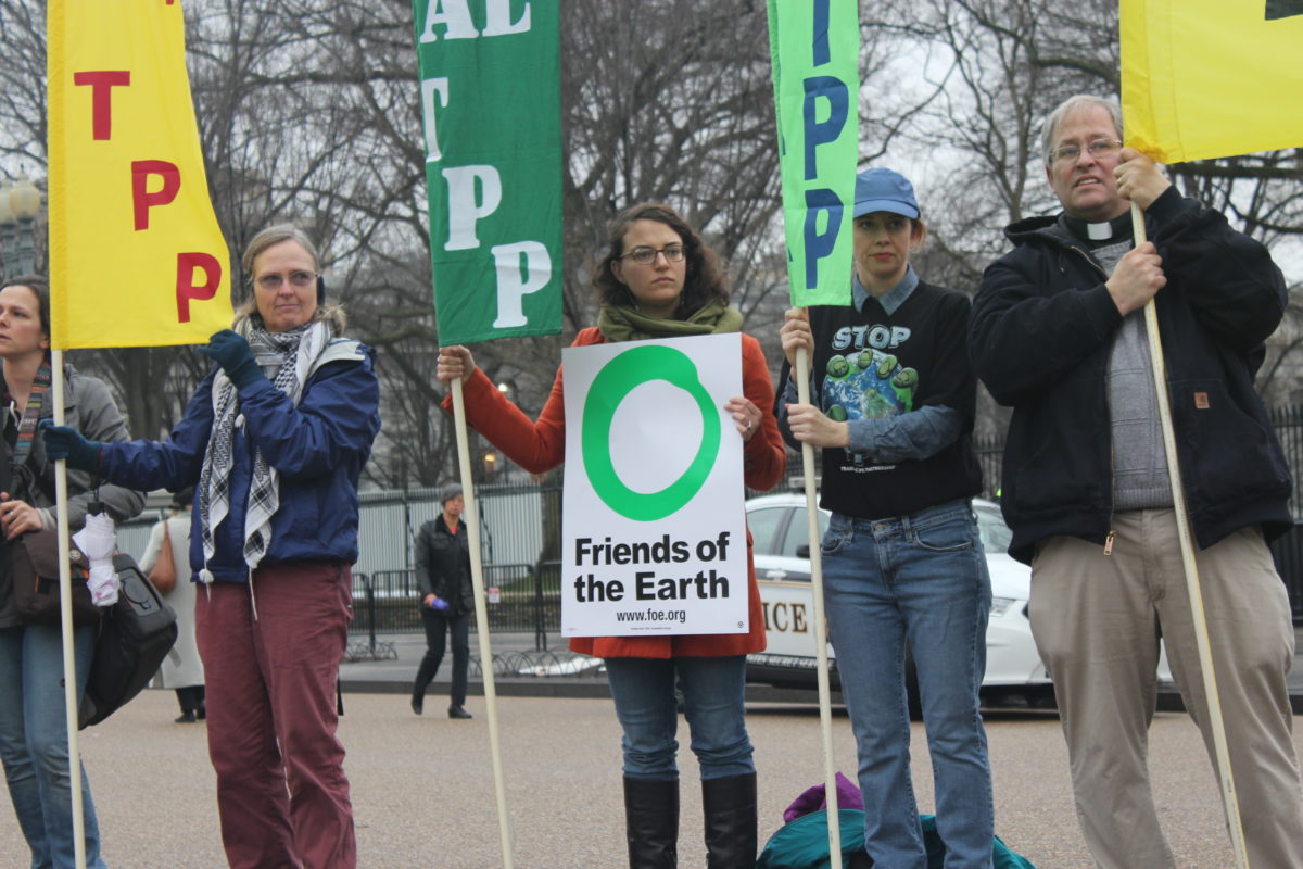 Four activists hold signs against the Trans Pacific Partnership trade deal and one holds a Friends of the Earth signs
