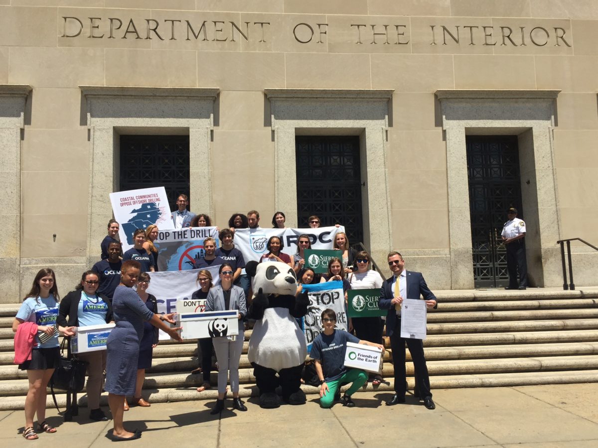 A group of activists outside of the Department of the Interior building with signs about stopping offshore drilling with a person in a panda costume