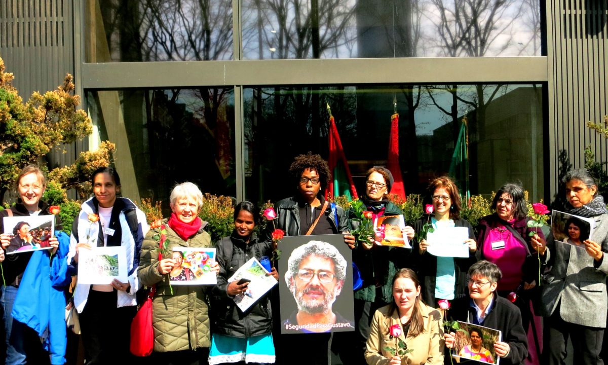 Activists standing outside of a building holding pictures memorializing Berta Caceres