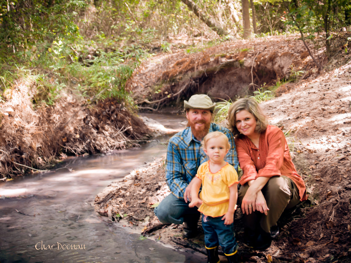 A family of three posing next to a river in the woods