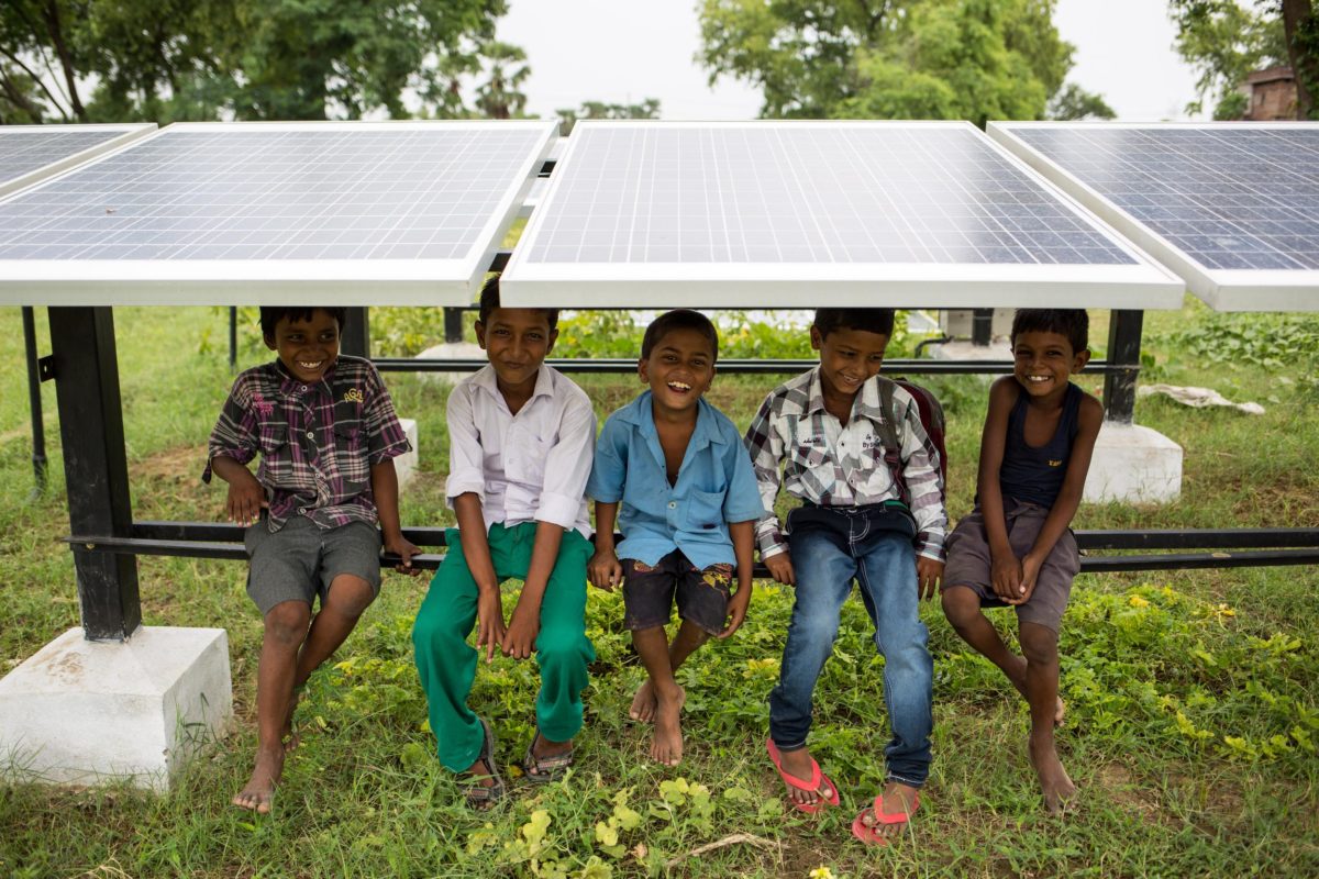 Five children sitting underneath a solar panel