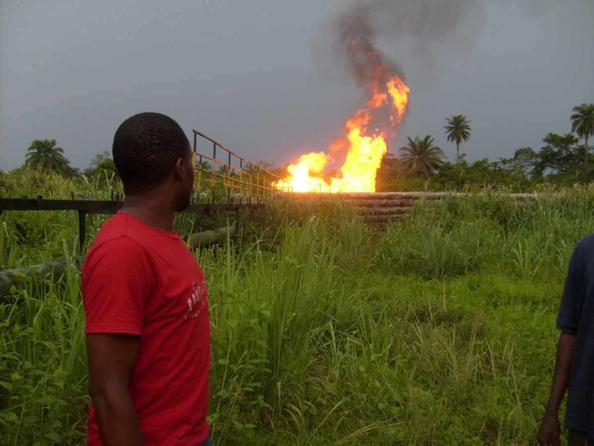 A man in a red shirt looking at a fire burning in a field in the distance