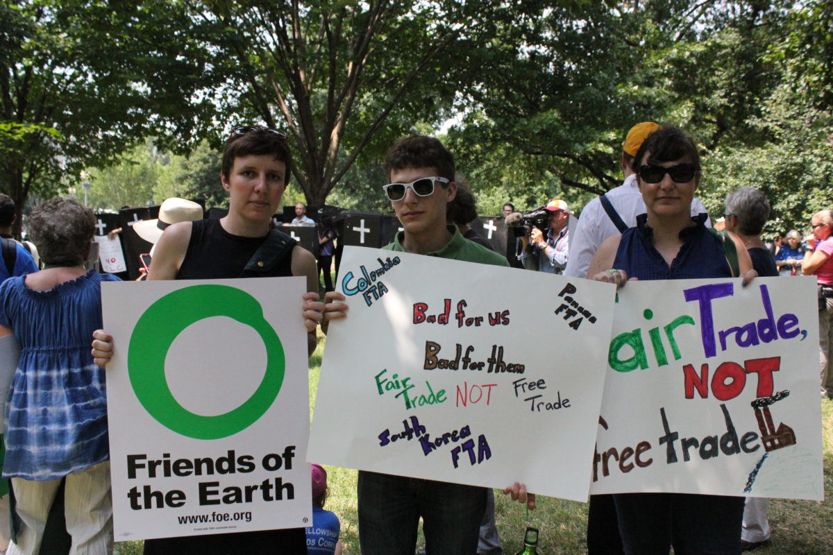 Three protestors holding signs supporting Friends of the Earth and fair trade