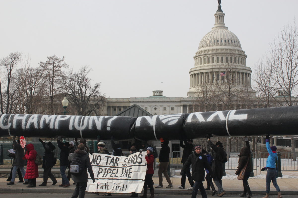 Activists outside of US Capitol Building protesting carrying a replica pipeline over their heads with a sign that says "No Tar Sands Pipeline Earth First!"