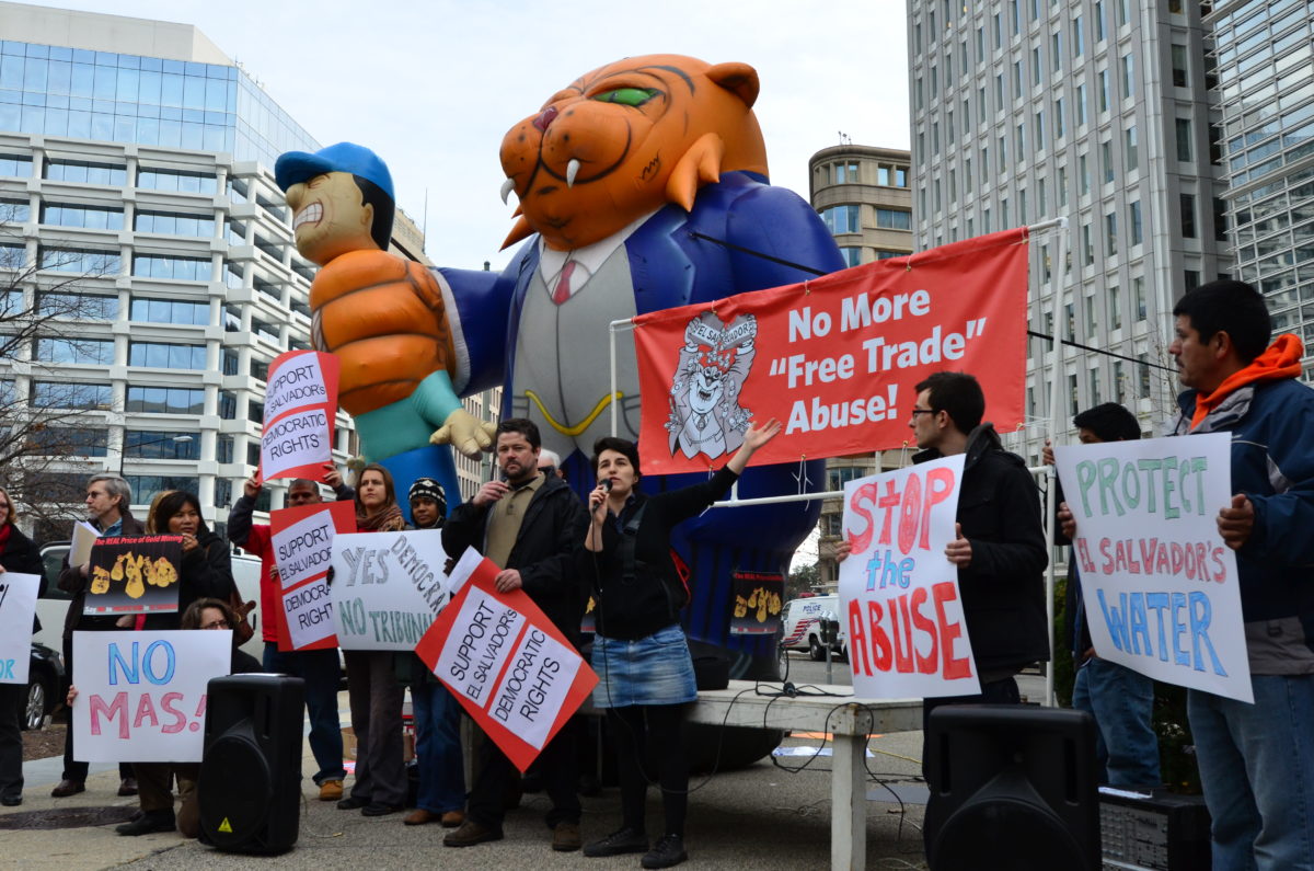 Protestors stand in front of an inflatable cat in a suit strangling an inflatable person