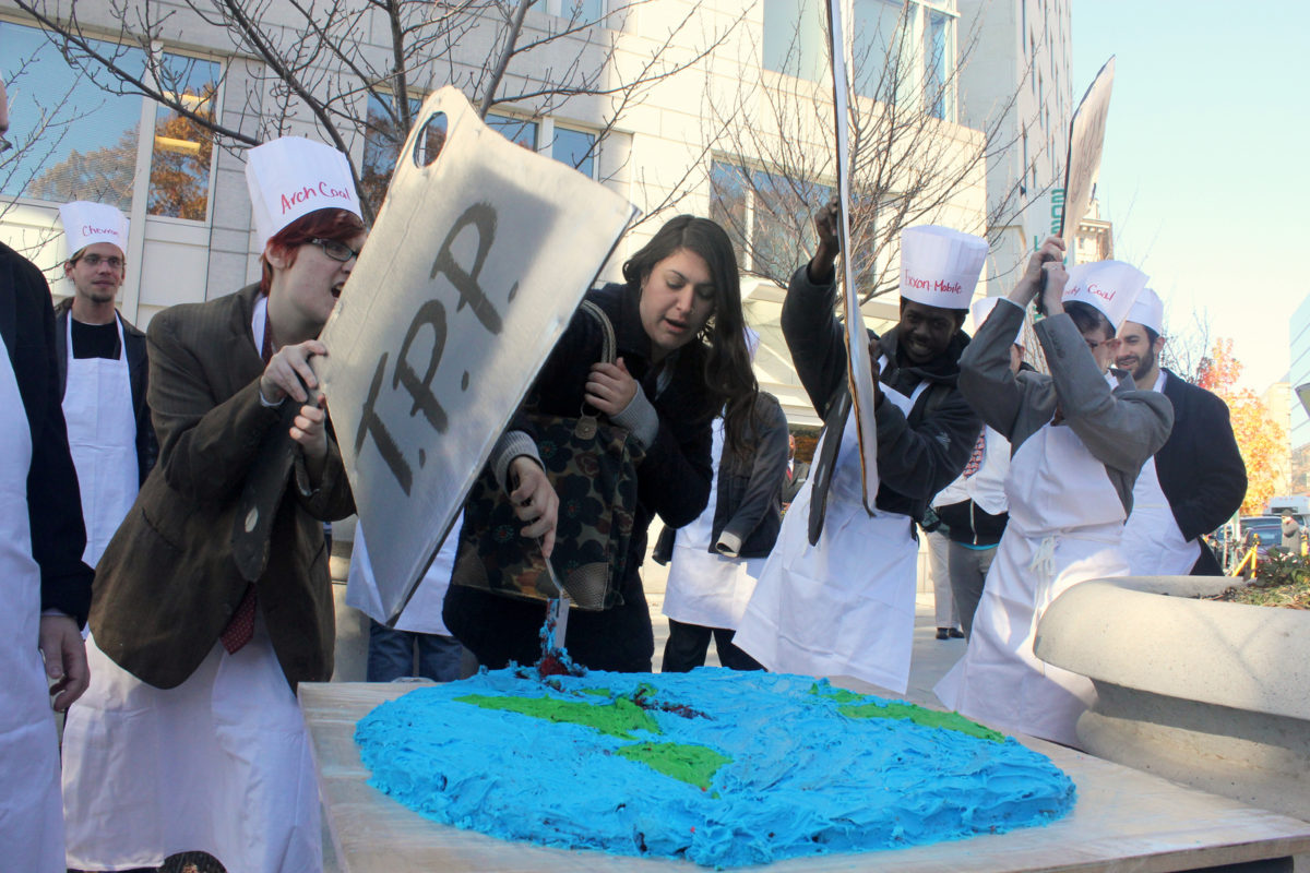Activists cutting a picture of the Earth with a cleaver that says TPP