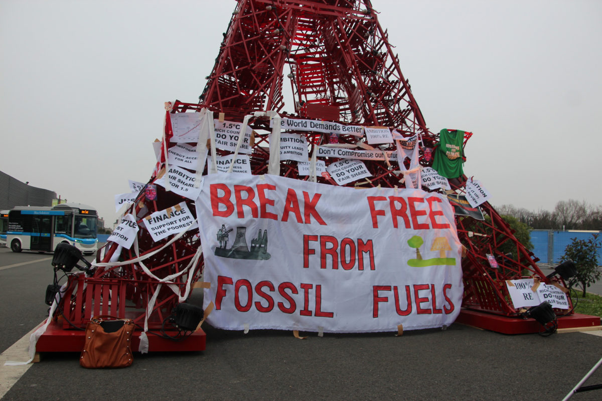 A makeshift oil rig at a protest with signs against funding fossil fuels