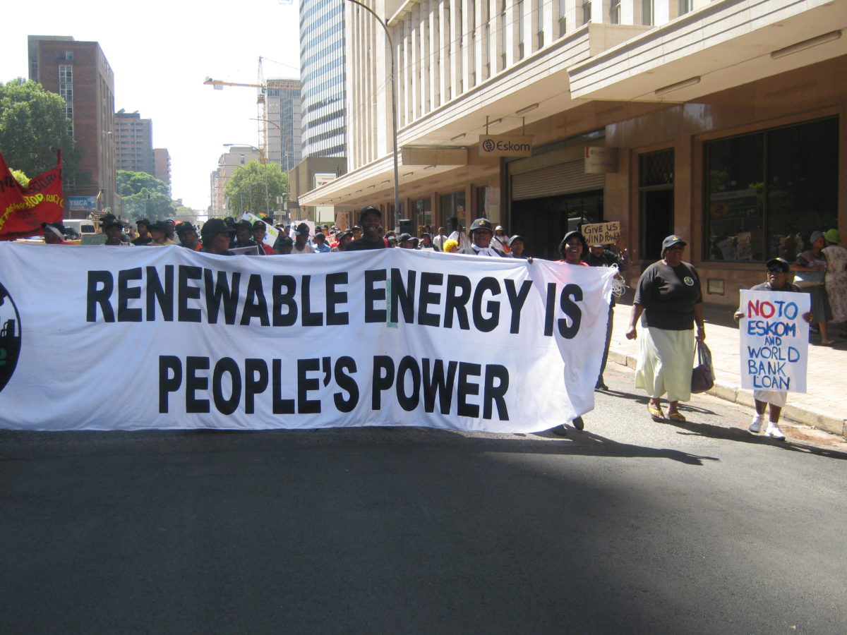 Activists marching and carrying a banner that says "Renewable Energy is People's Power"