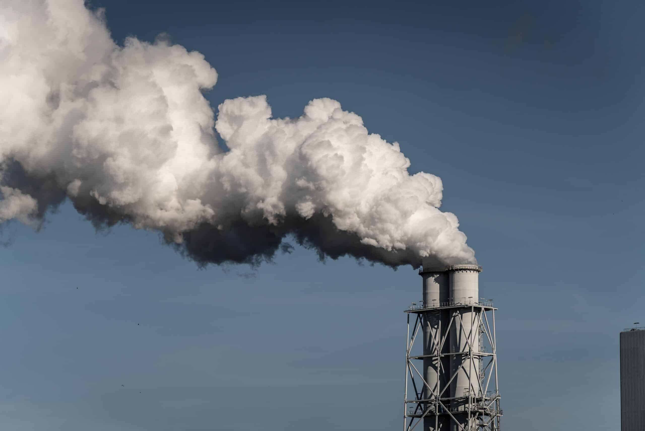 May contain two industrial chimneys emitting white smoke against a blue sky.