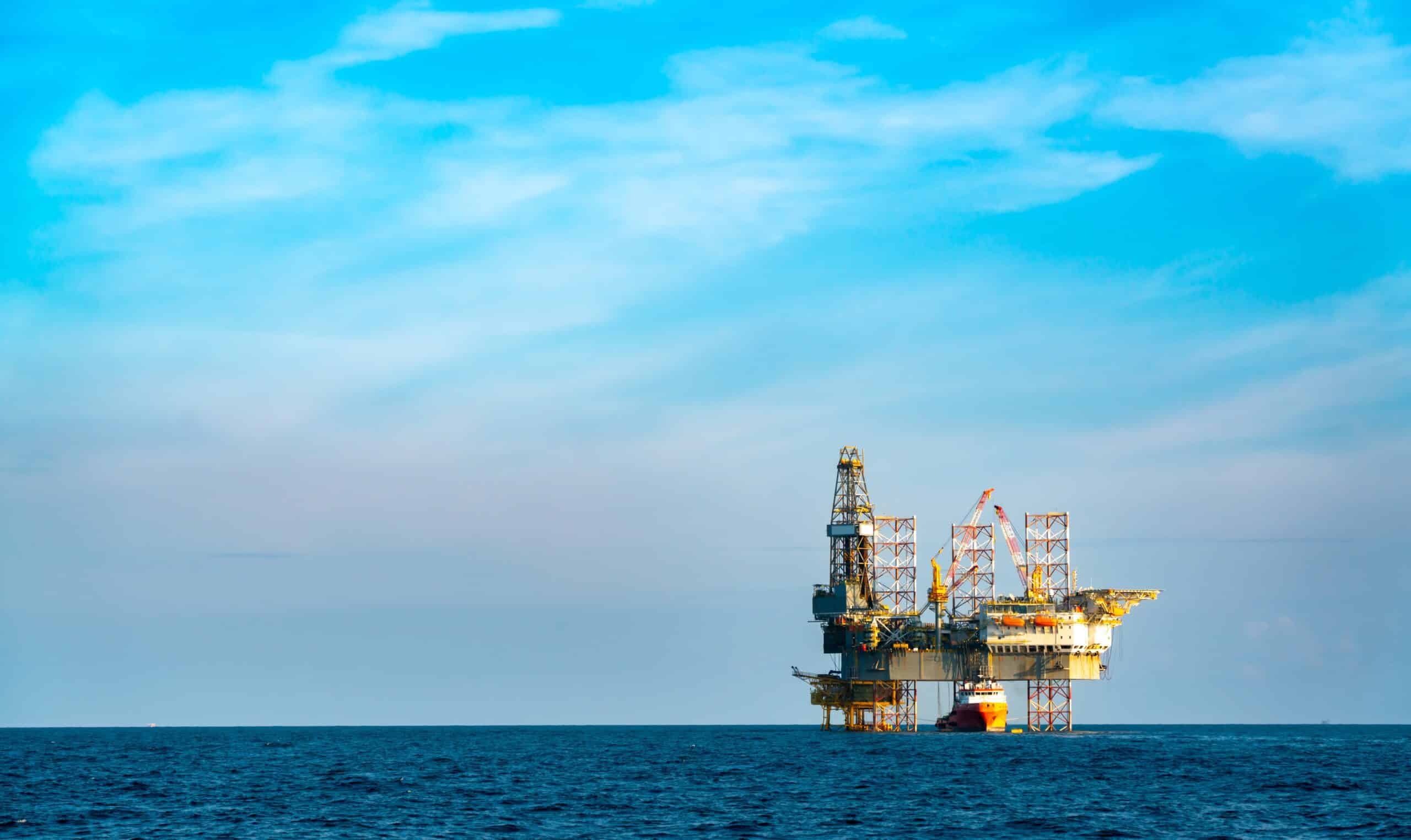 May contain an oil rig on the ocean under a blue sky.