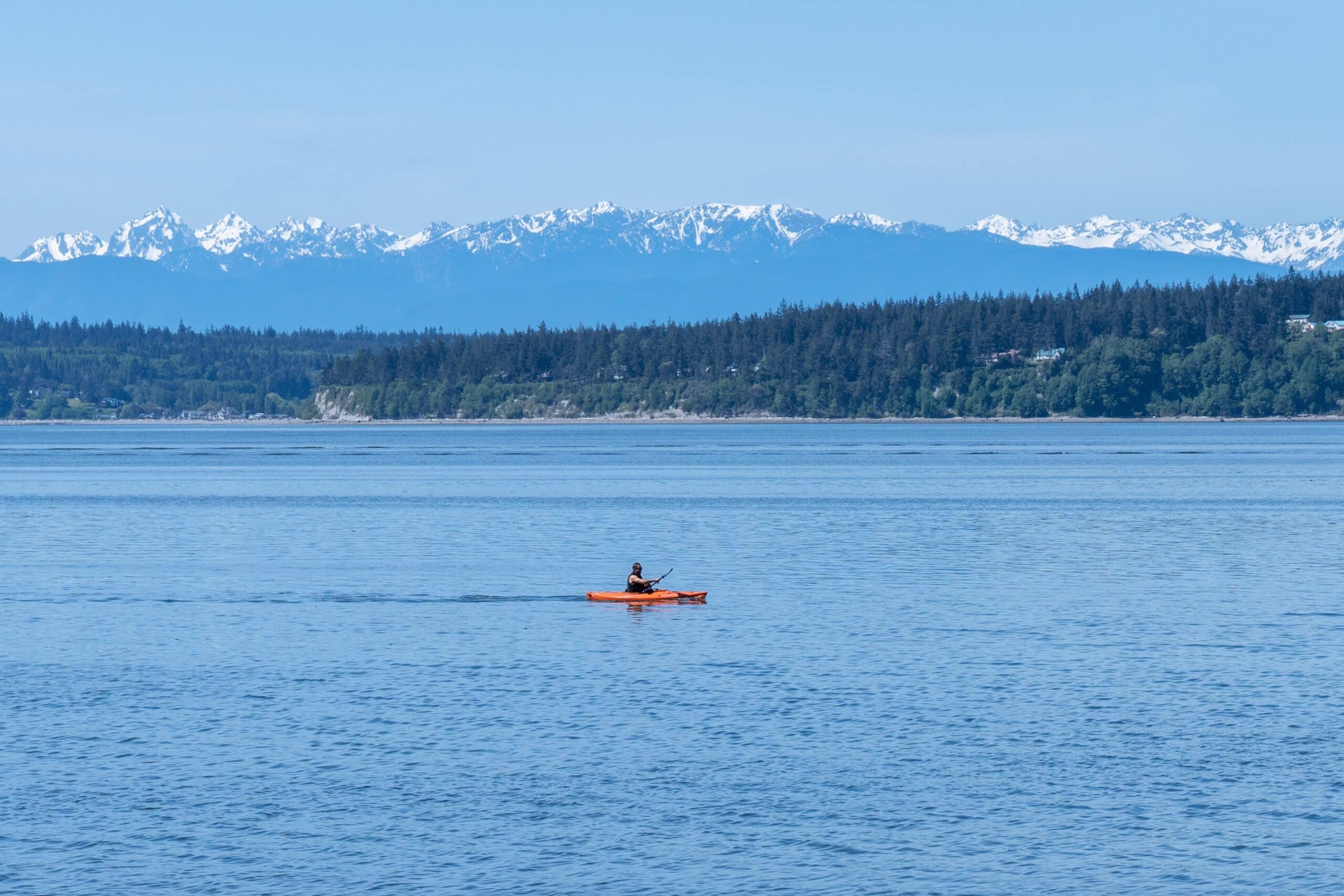 May contain a person kayaking on the water with snowy mountains in the background.