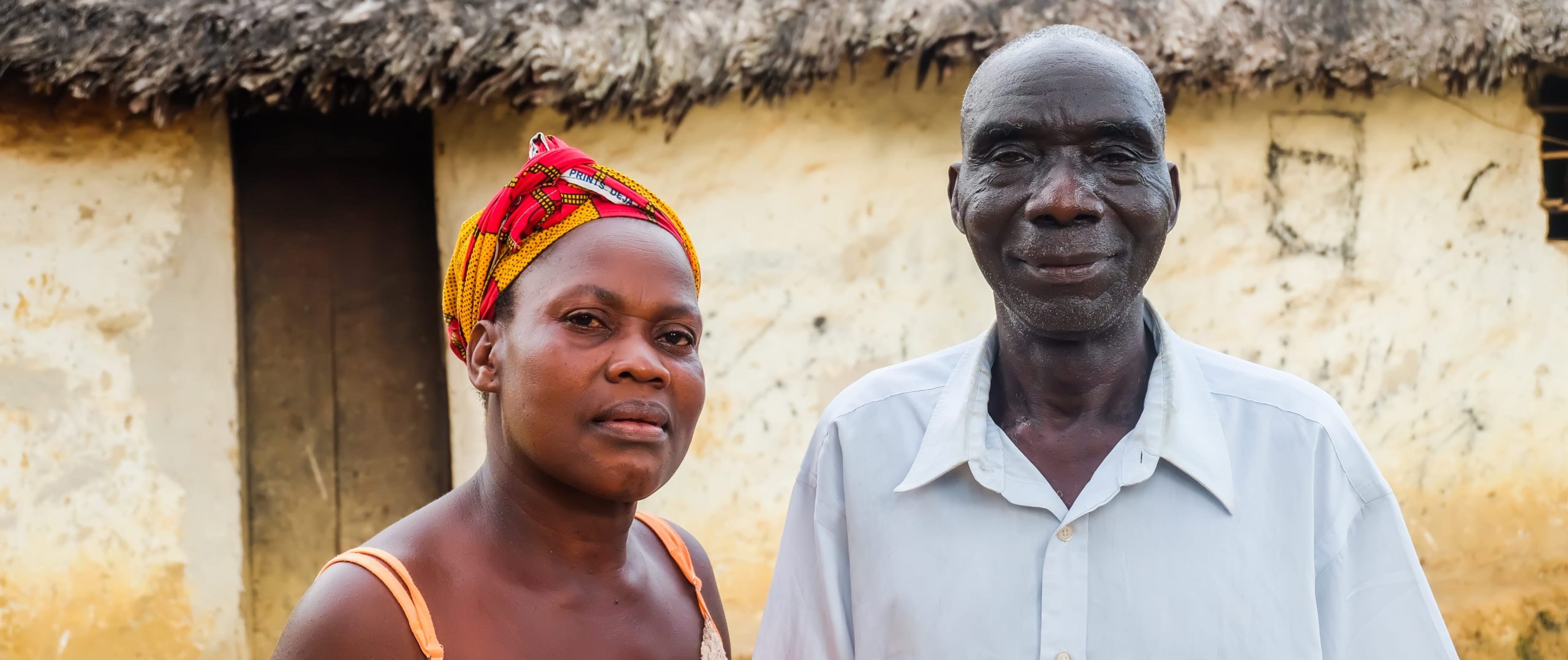 A man and a woman standing in front of a hut