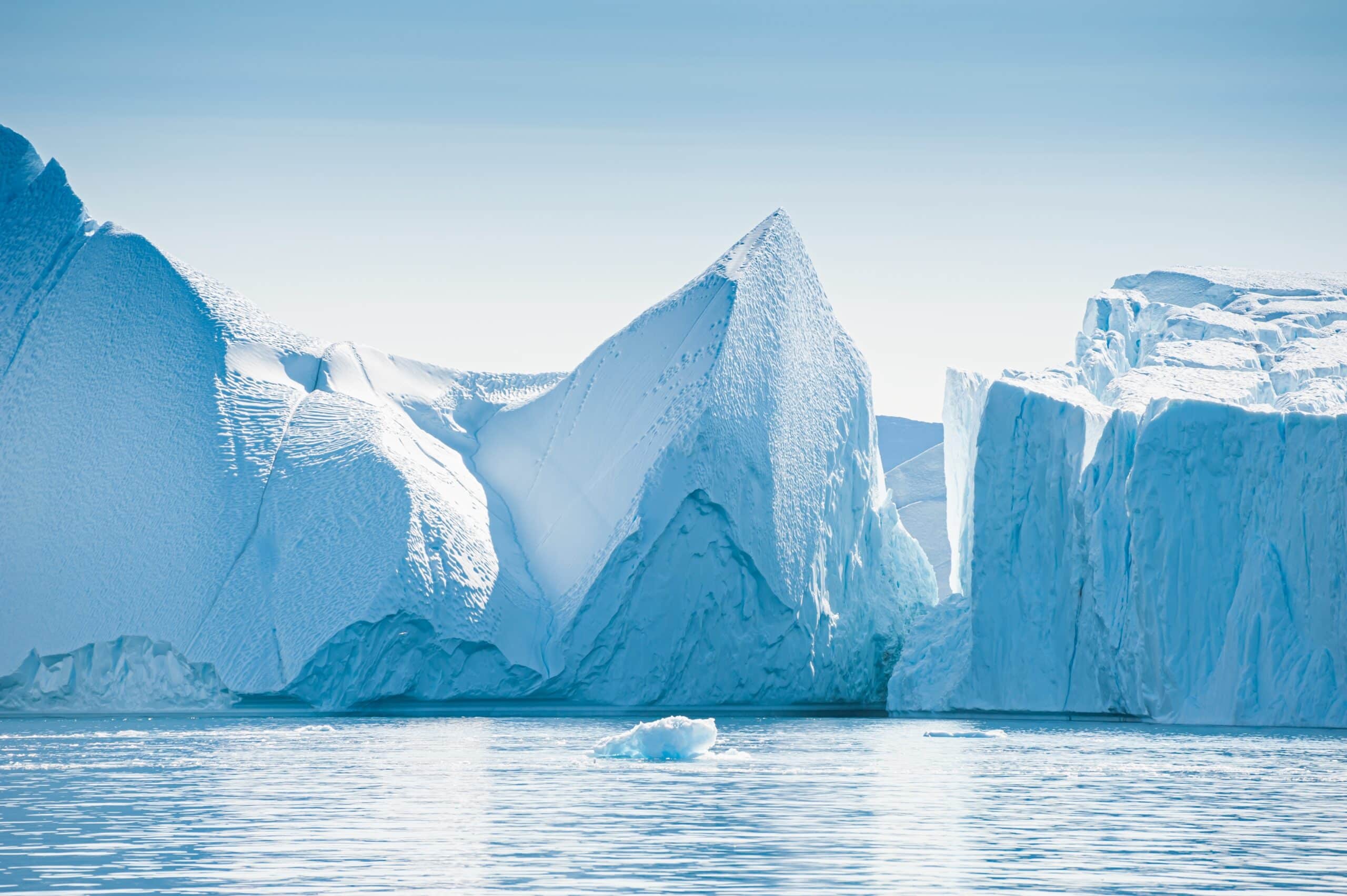 May contain large icebergs in calm blue water under a clear sky.