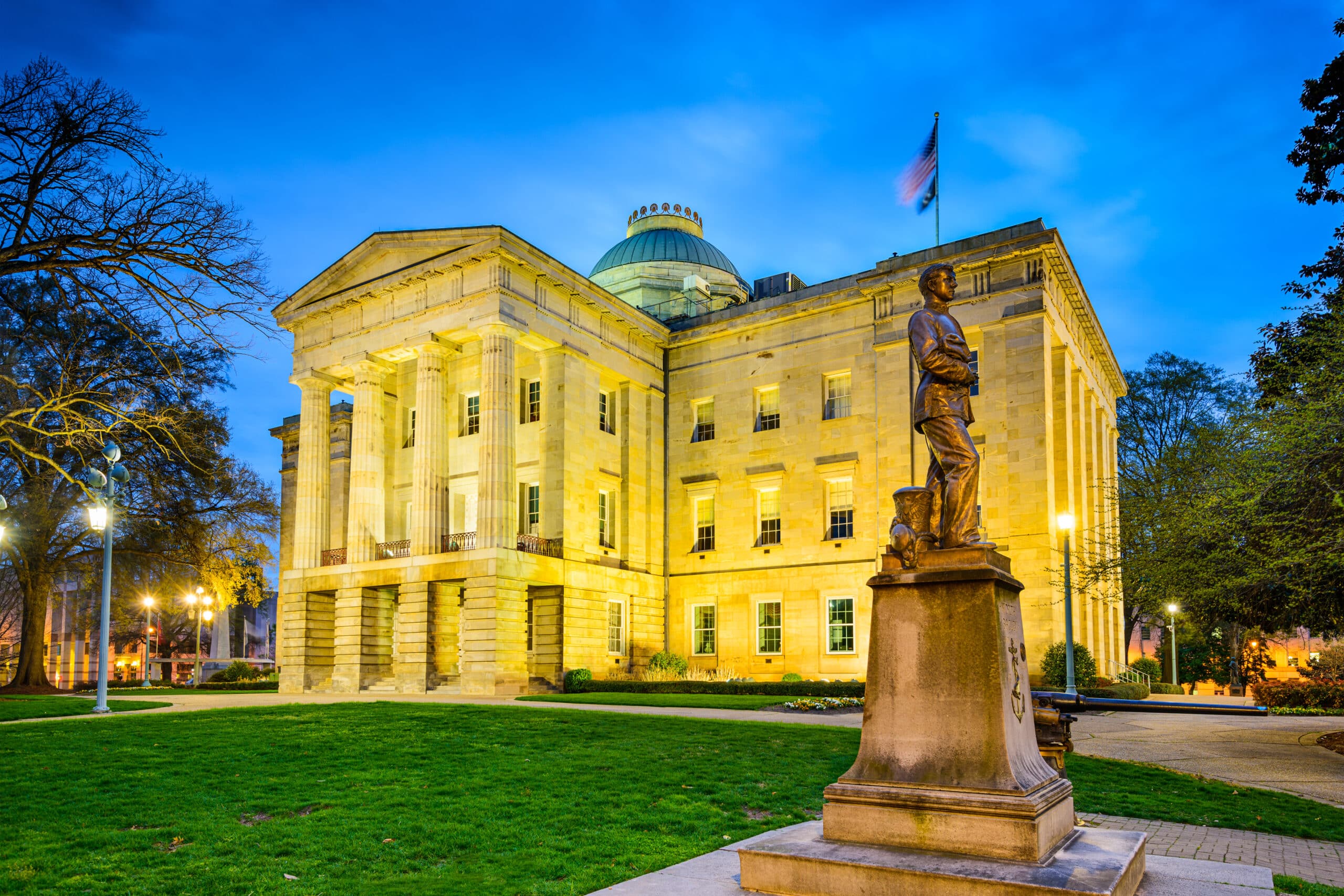 May contain a statue of a person in front of a large, lit building at dusk.