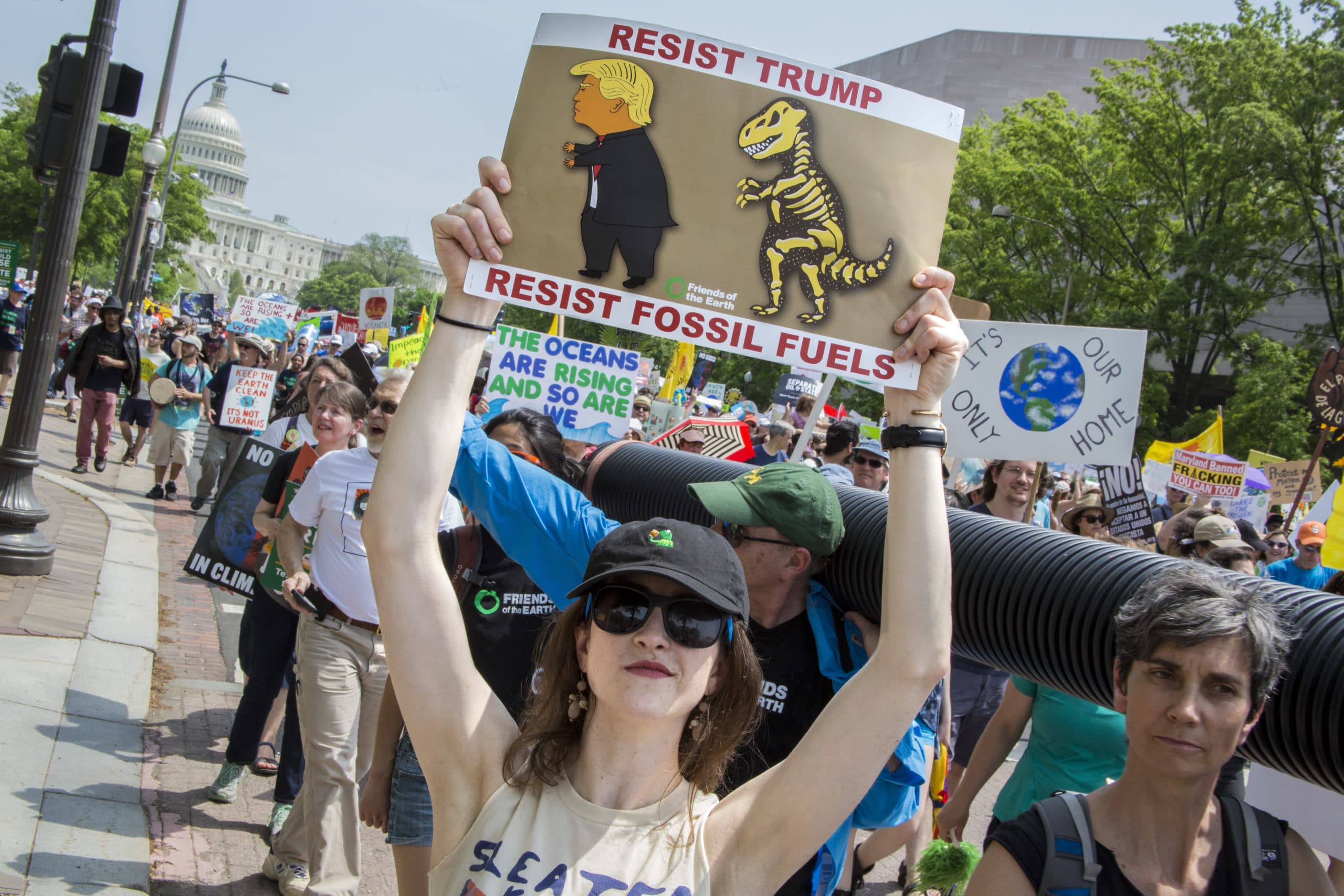 An activist in a march near the US Capitol Building holding a sign against President Trump and fossil fuels