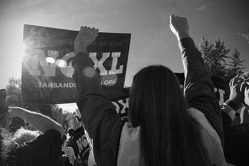 An activists standing with hands raised in front of a sign against the Keystone Pipeline