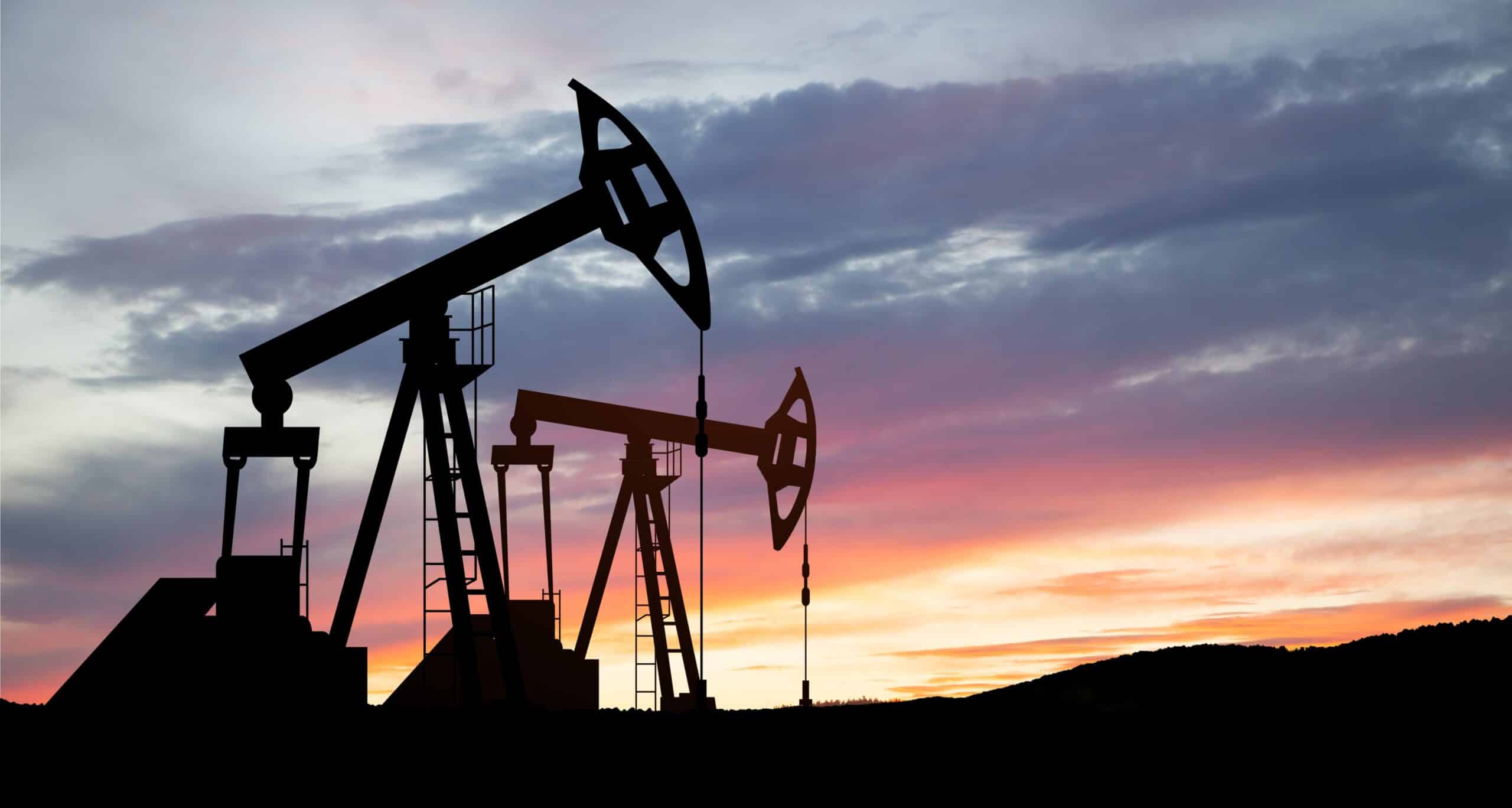 May contain two oil pump jacks silhouetted against a colorful sunset sky.