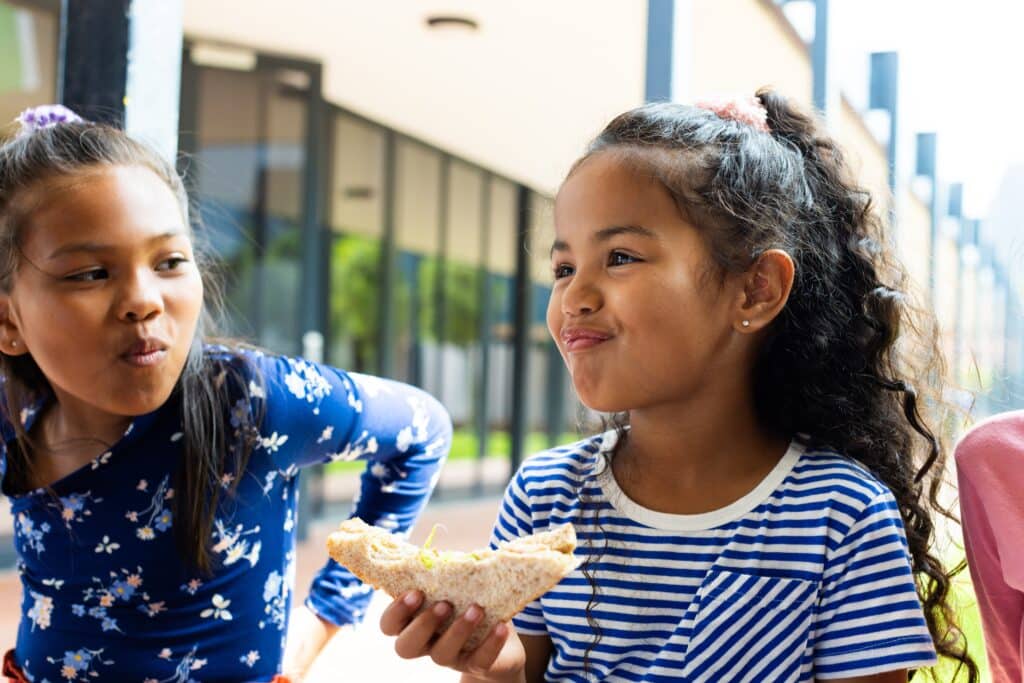 May contain two people. One person wears a blue floral shirt and another person wears a blue striped shirt and holds a sandwich.