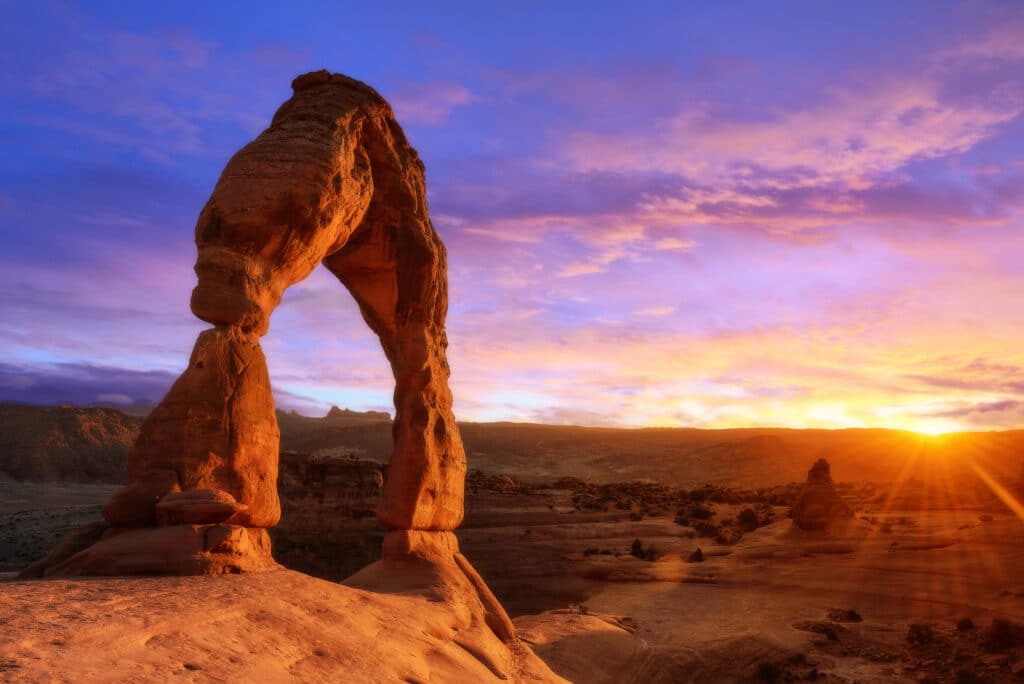 May contain two people standing on a sandstone arch at sunset.