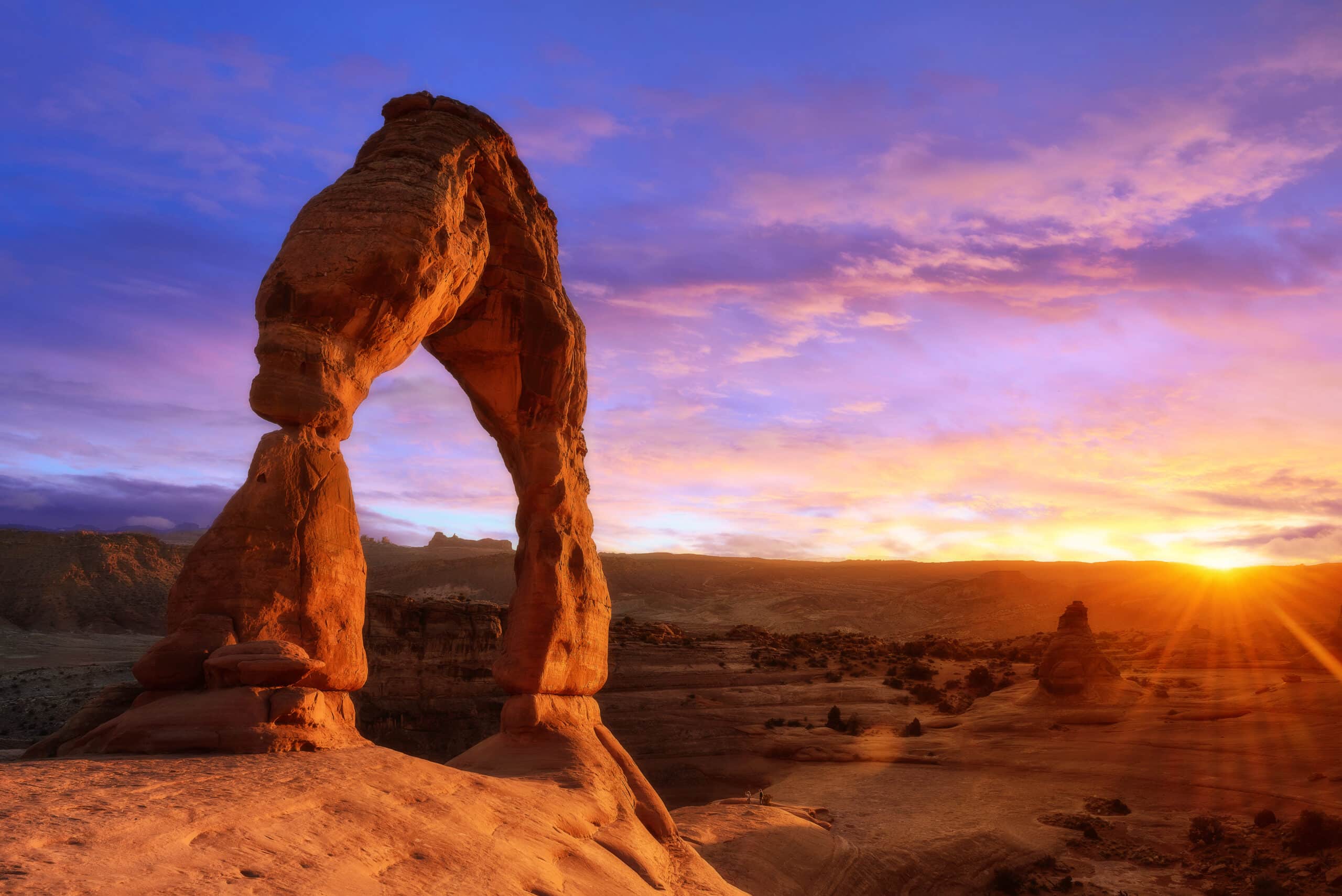 May contain two people standing on a sandstone arch at sunset.