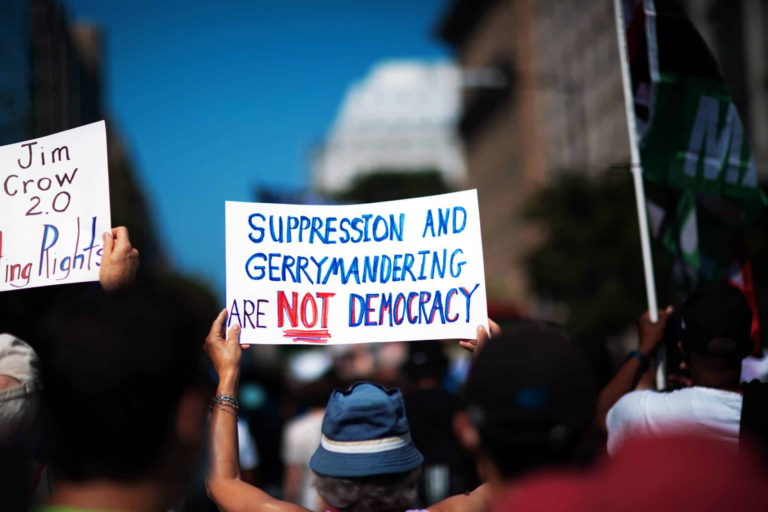 May contain people holding signs that say "Jim Crow 2.0" and "SUPPRESSION AND GERRYMANDERING ARE NOT DEMOCRACY".