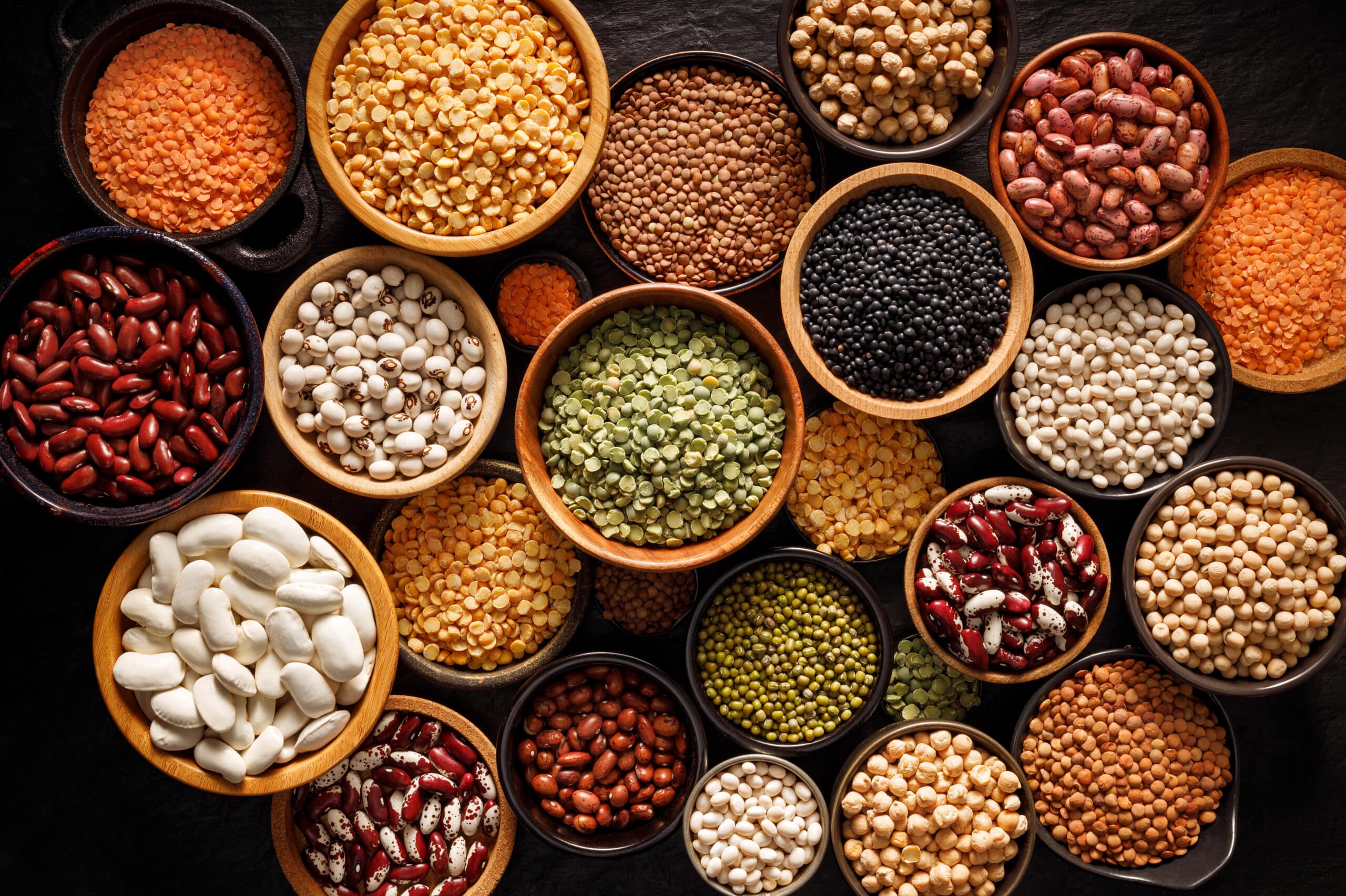 May contain bowls of various legumes and lentils on a dark surface.