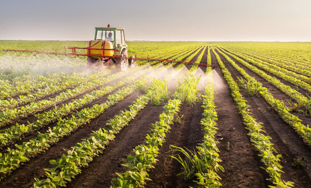 May contain one person driving a tractor spraying a field of crops.