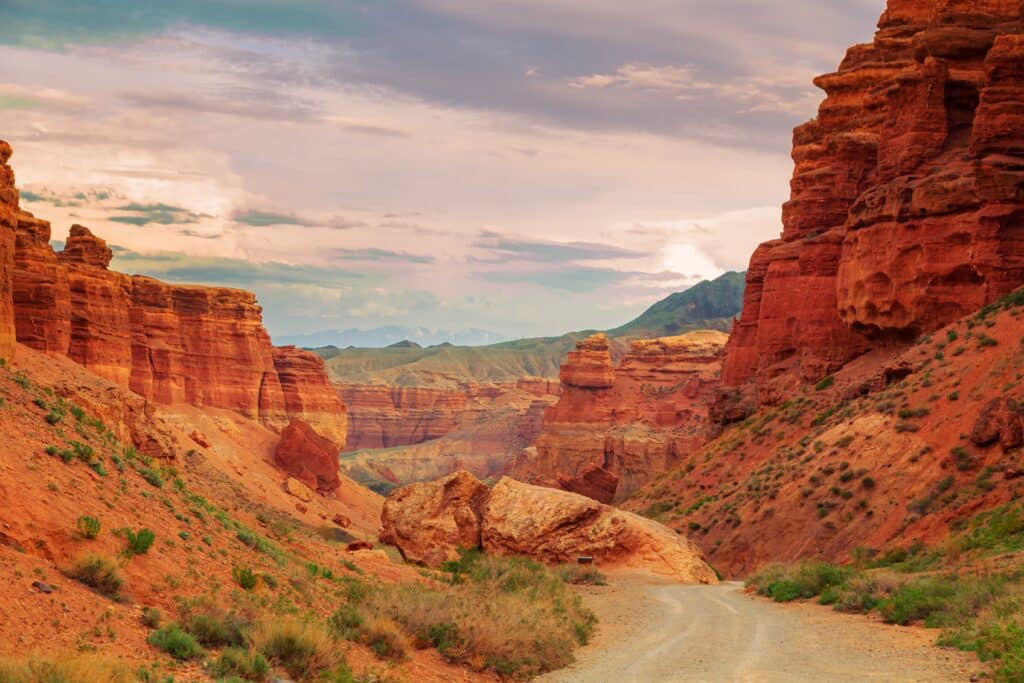 May contain a dirt road winding through a canyon of red rock formations under a cloudy sky.