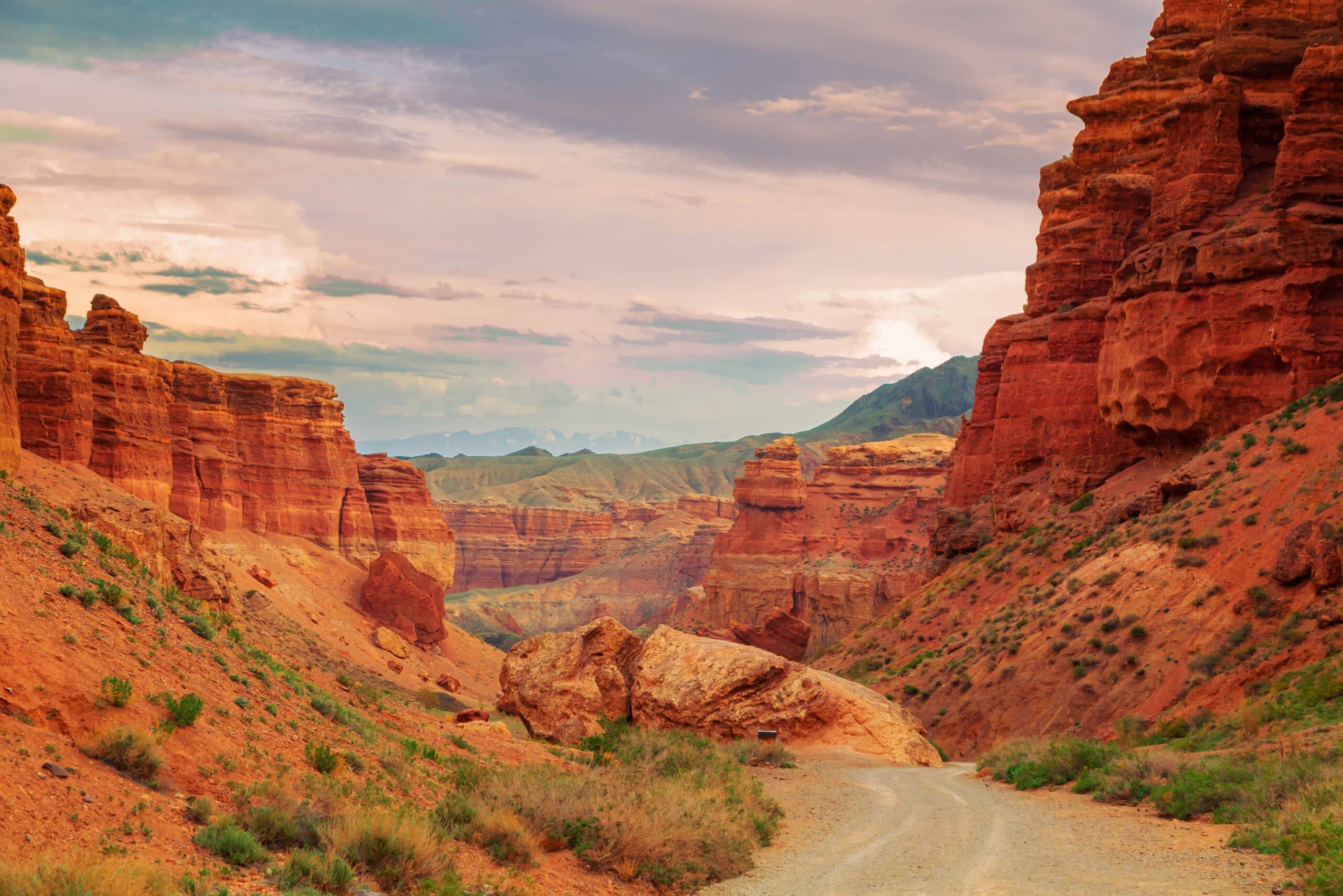 May contain a dirt road winding through a canyon of red rock formations under a cloudy sky.