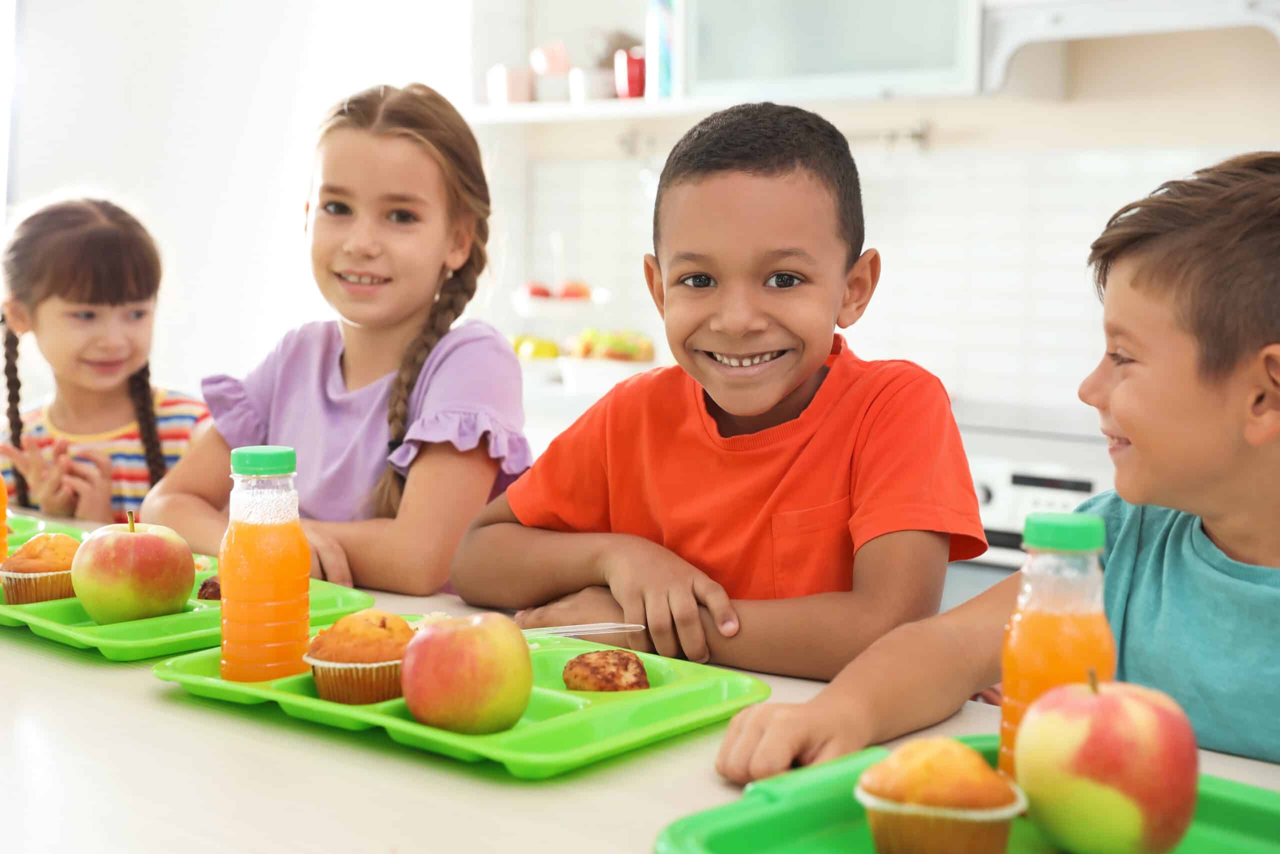 May contain four people eating lunch at a table with juice and apples.