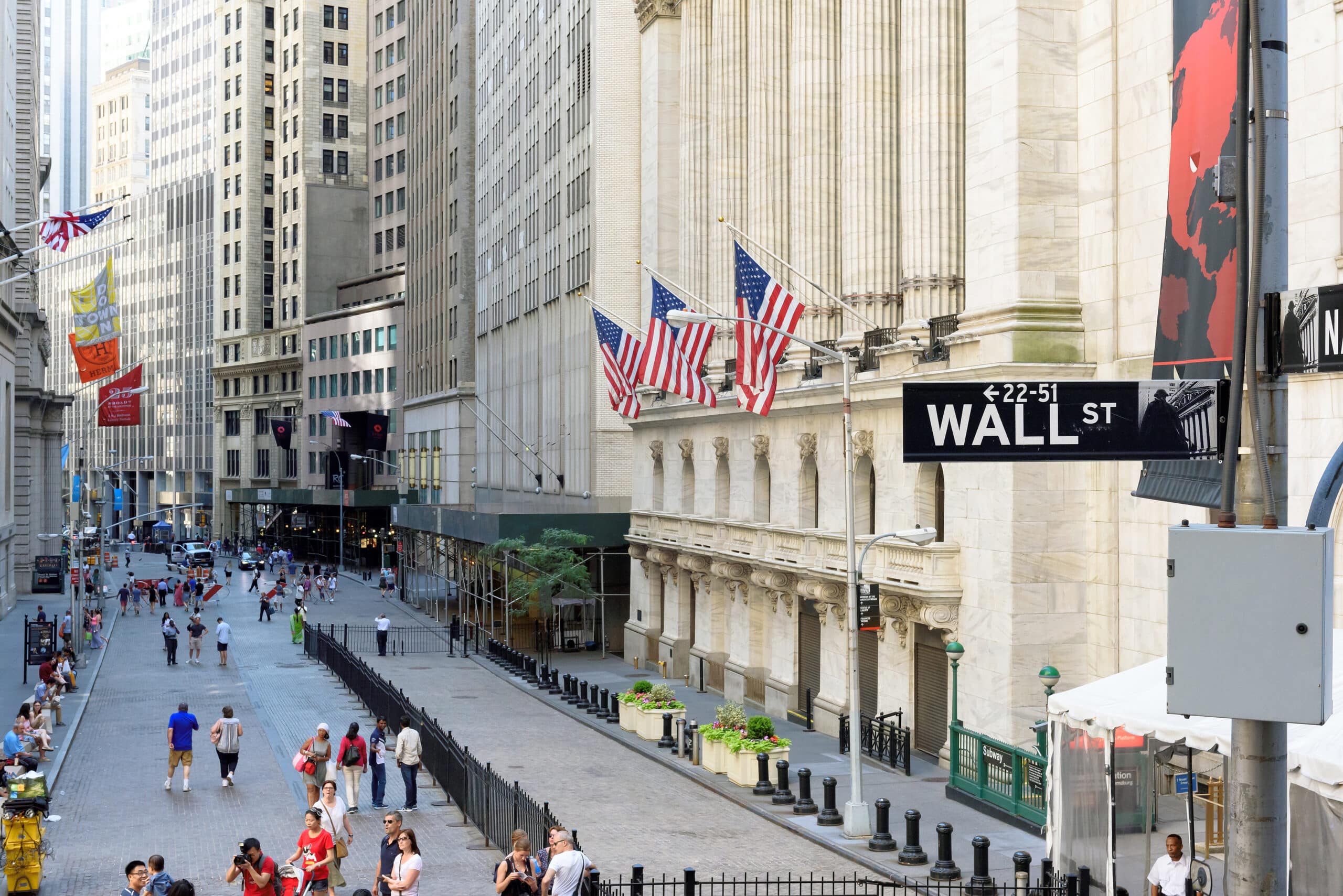May contain many people walking on a street with tall buildings and flags.