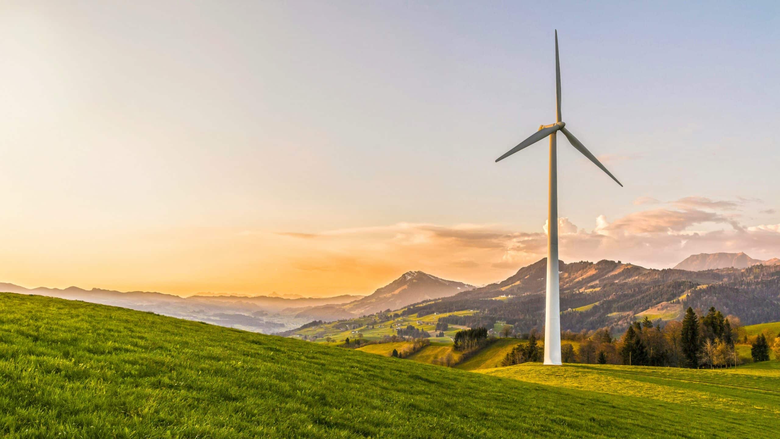 May contain a wind turbine on a green hill at sunset.