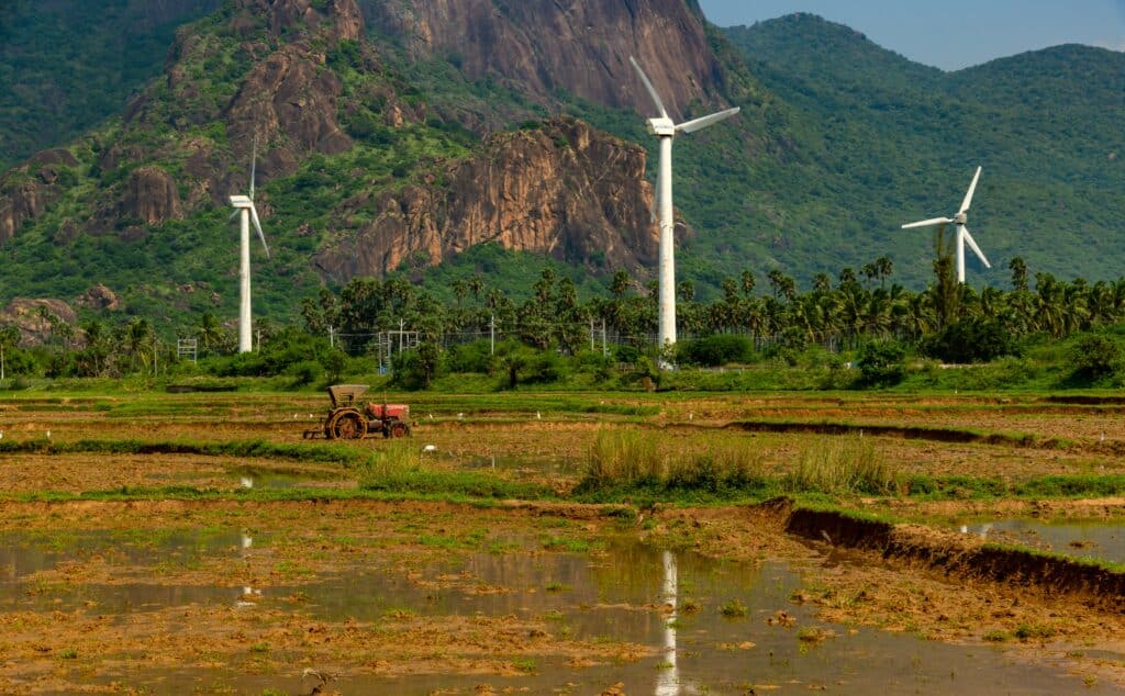 May contain three wind turbines and a tractor in a field.
