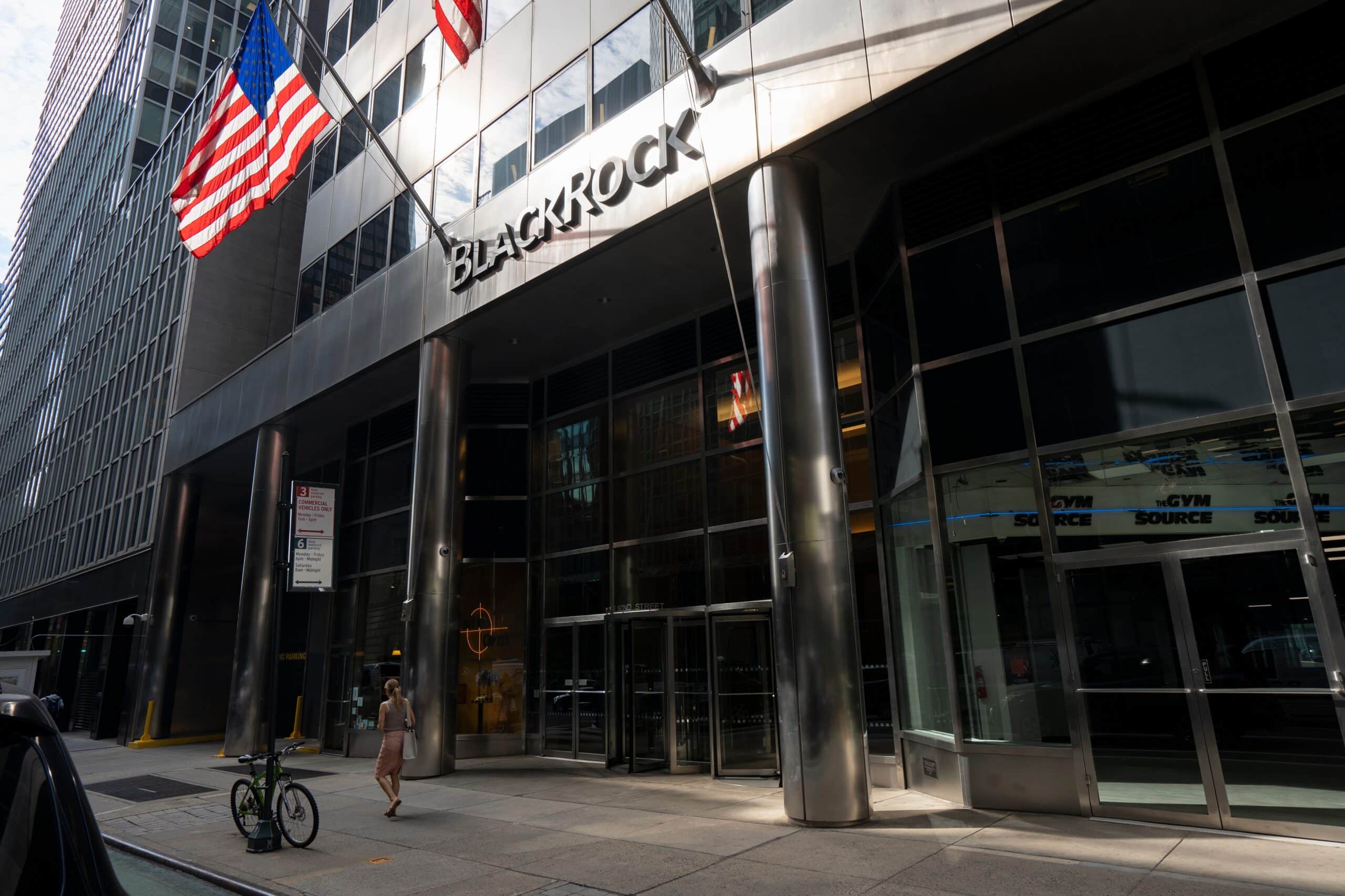May contain a person walking by a BlackRock building with US flags.