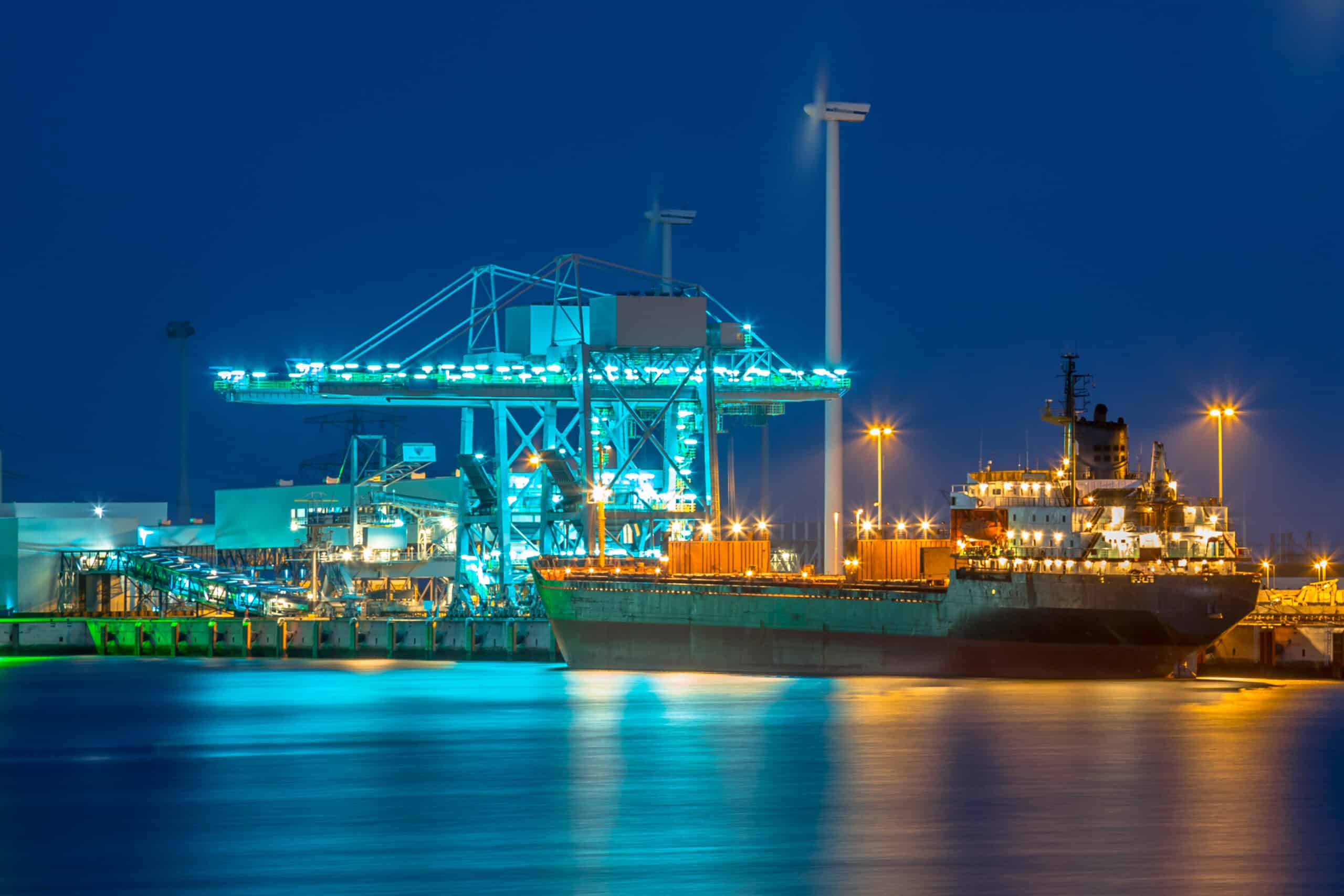 May contain a large cargo ship and cranes at a port at night.