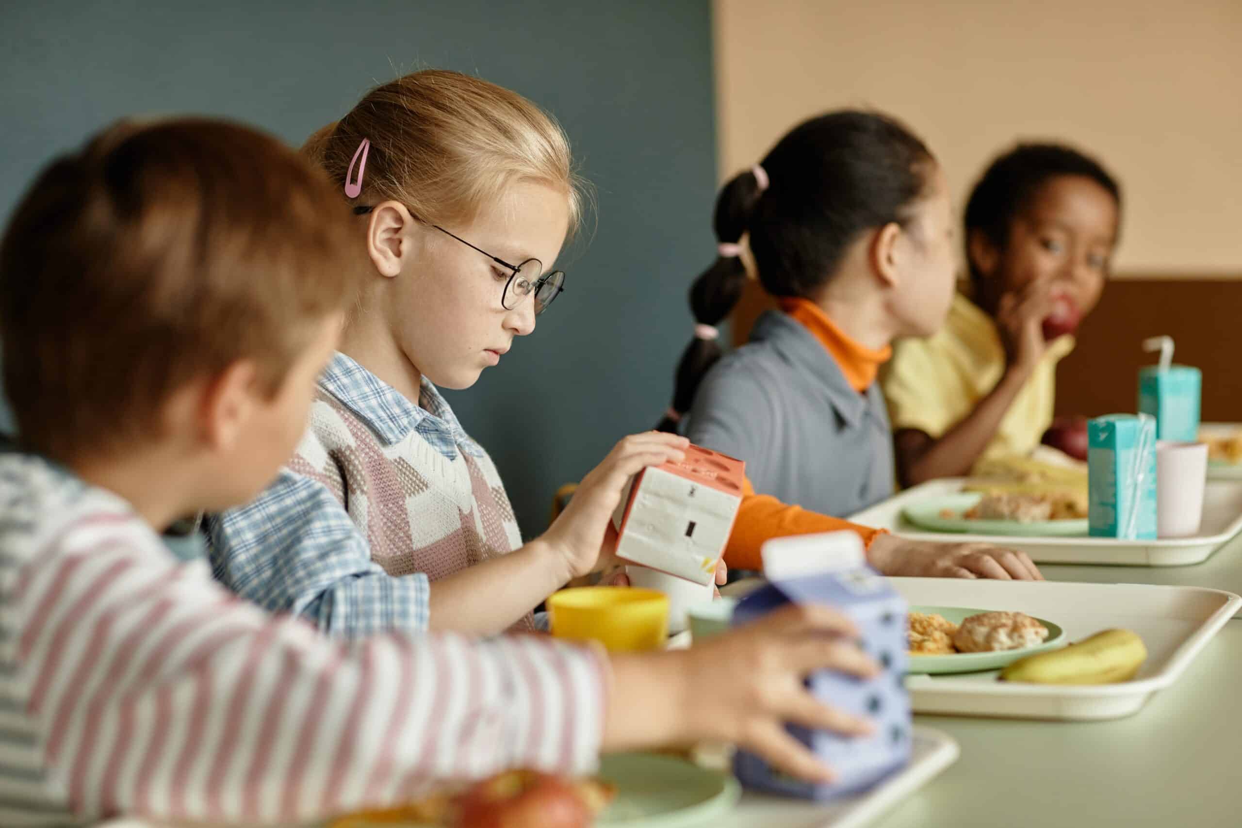May contain four people sitting at lunch tables with food trays.
