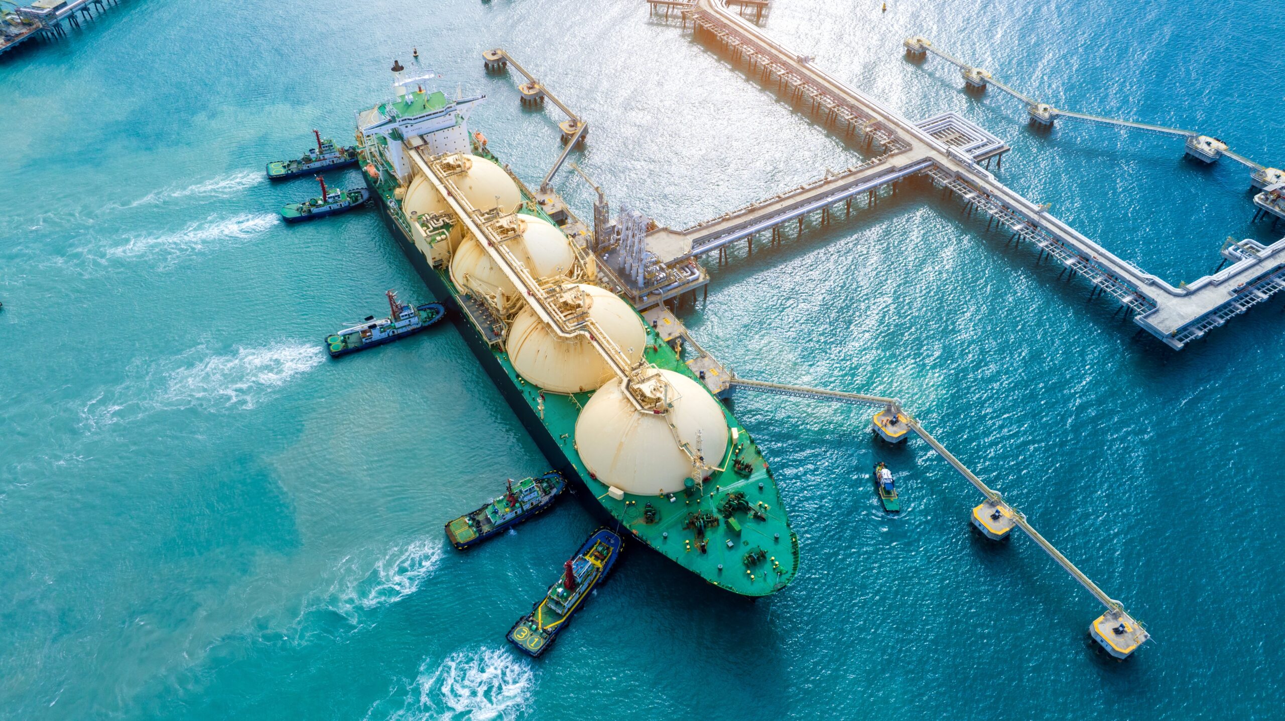 May contain an LNG carrier ship being assisted by multiple tugboats.