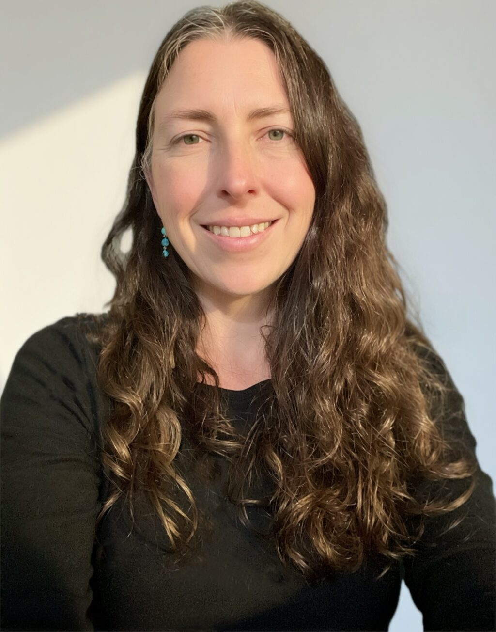 May contain one person smiling, wearing a black shirt and turquoise earrings.